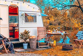 A camper trailer parked beside a serene lake, surrounded by trees and reflecting water A camper trailer parked beside a serene lake, surrounded by trees and reflecting water